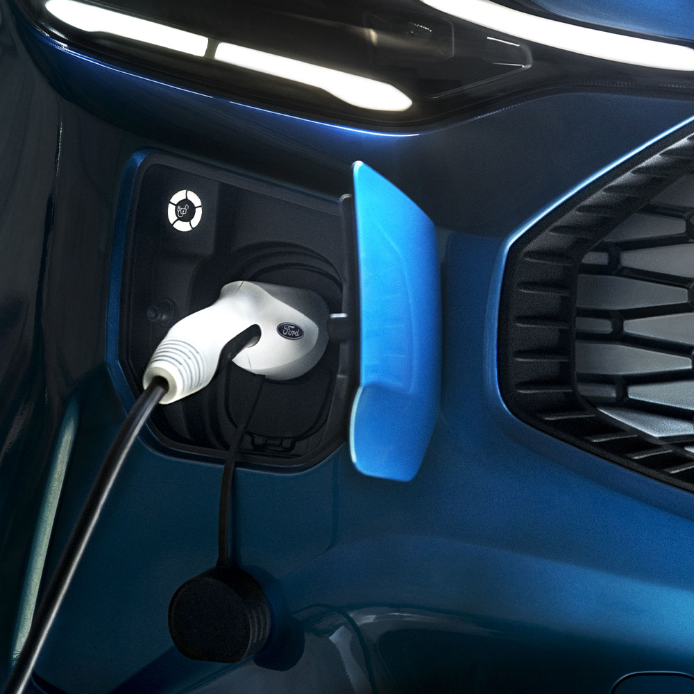 Una porta di ricarica per veicoli elettrici con un caricatore per auto elettriche collegato con alle spalle un veicolo Ford blu.
