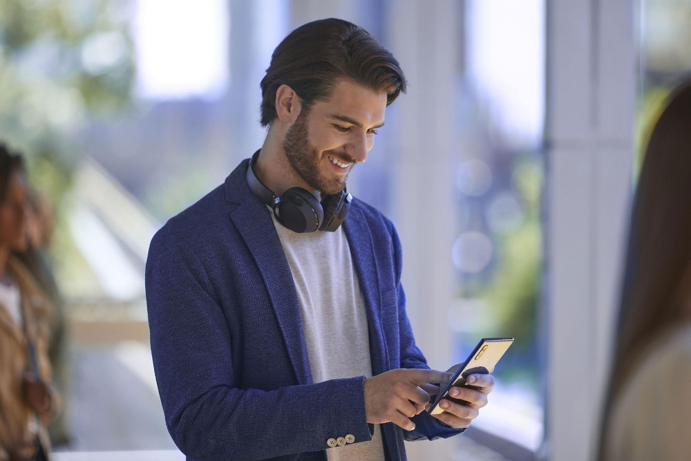 Una persona sorridente che guarda il proprio telefono, con le cuffie al collo.