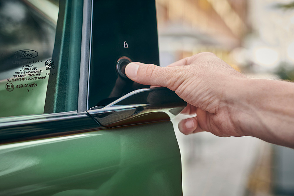 Primo piano di una mano che aziona il sistema E-Latch premendo un pulsante sulla portiera di un Ford Mustang Mach-E in eruption green.