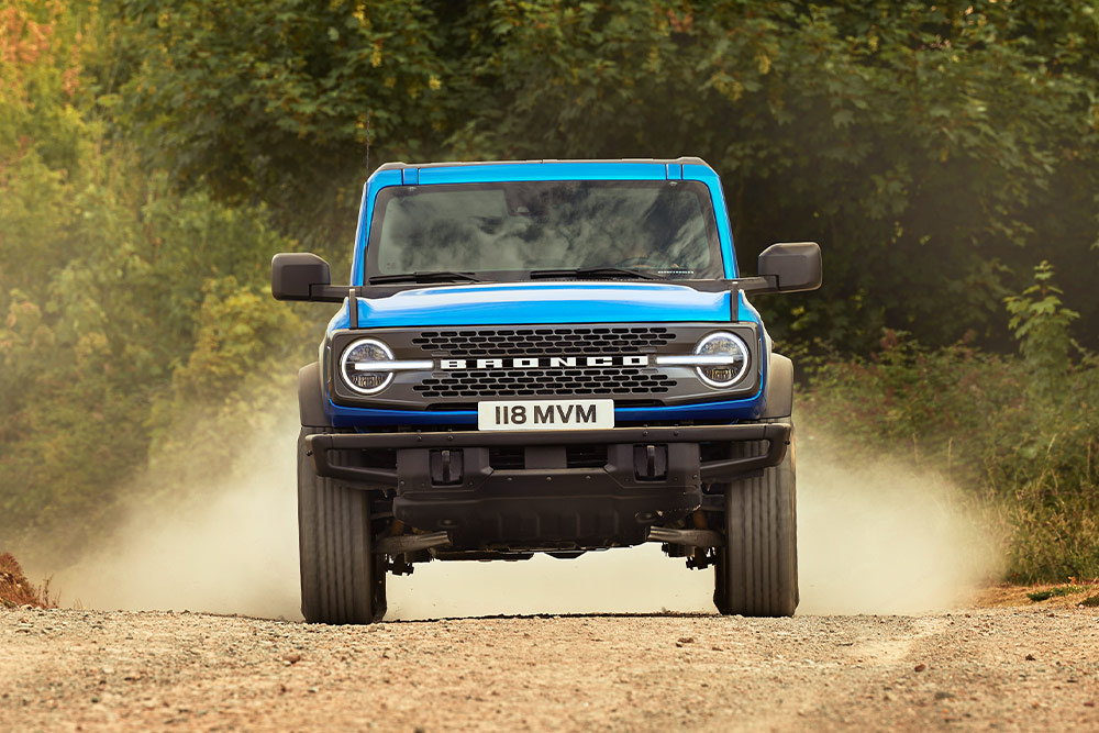 Vista frontale di un Ford Bronco blu che percorre una strada sterrata. 