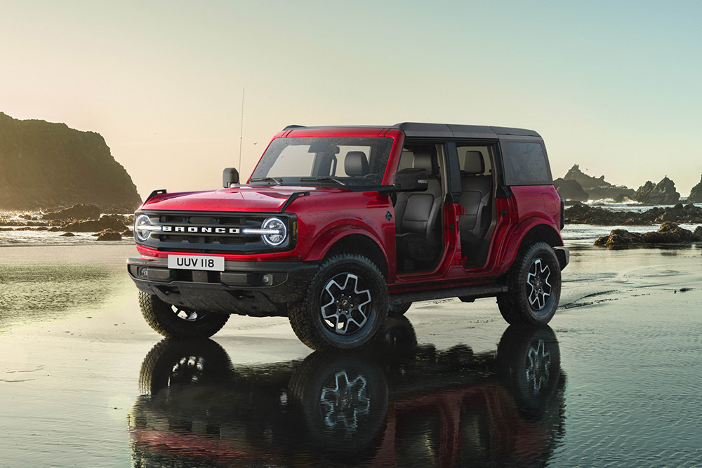 Vista laterale di un Ford Bronco rosso senza portiere parcheggiato su una spiaggia bagnata.