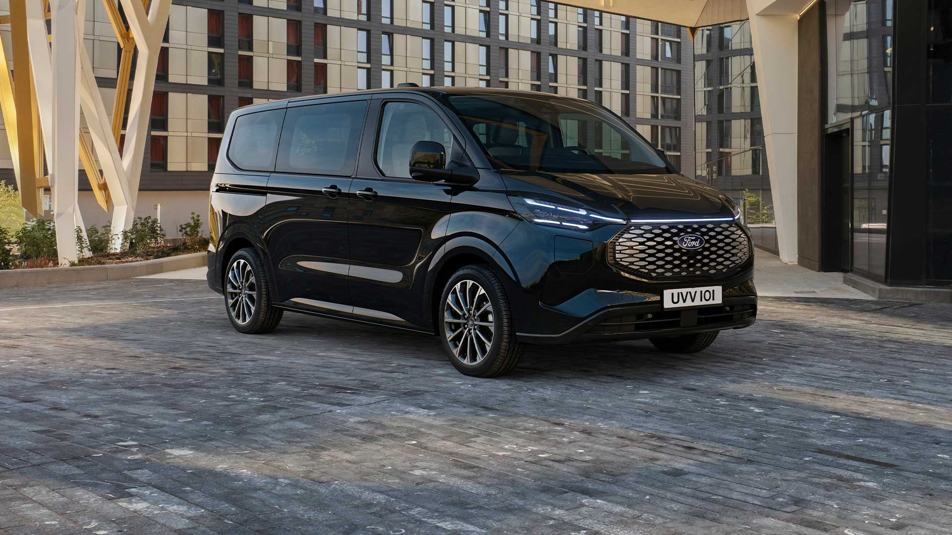 Un Ford E-Tourneo Custom nero parcheggiato di fronte a un edificio moderno.