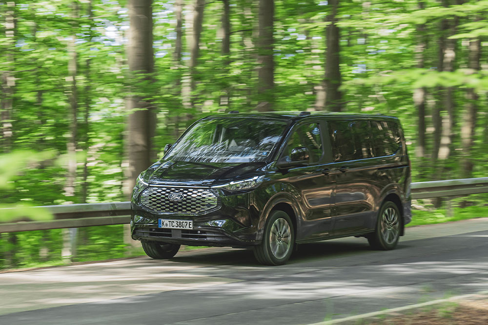 Un Ford E-Tourneo Custom nero percorre un viale alberato.