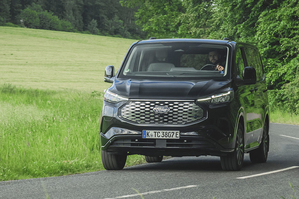 Un Ford E-Tourneo Custom nero percorre una strada di campagna.