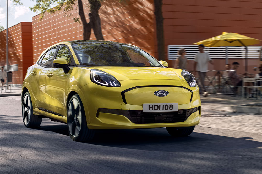 Vista frontale di un Ford Puma Gen-E® elettrico giallo che percorre una strada cittadina.