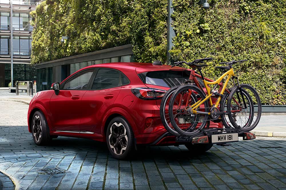 Ford Puma rossa parcheggiata in un contesto urbano con due biciclette montate su un portabici posteriore. 
