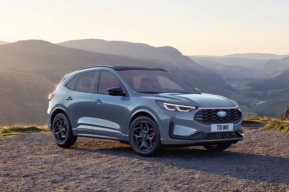 Una Ford Kuga grigia parcheggiata su una strada sterrata di montagna al tramonto.
