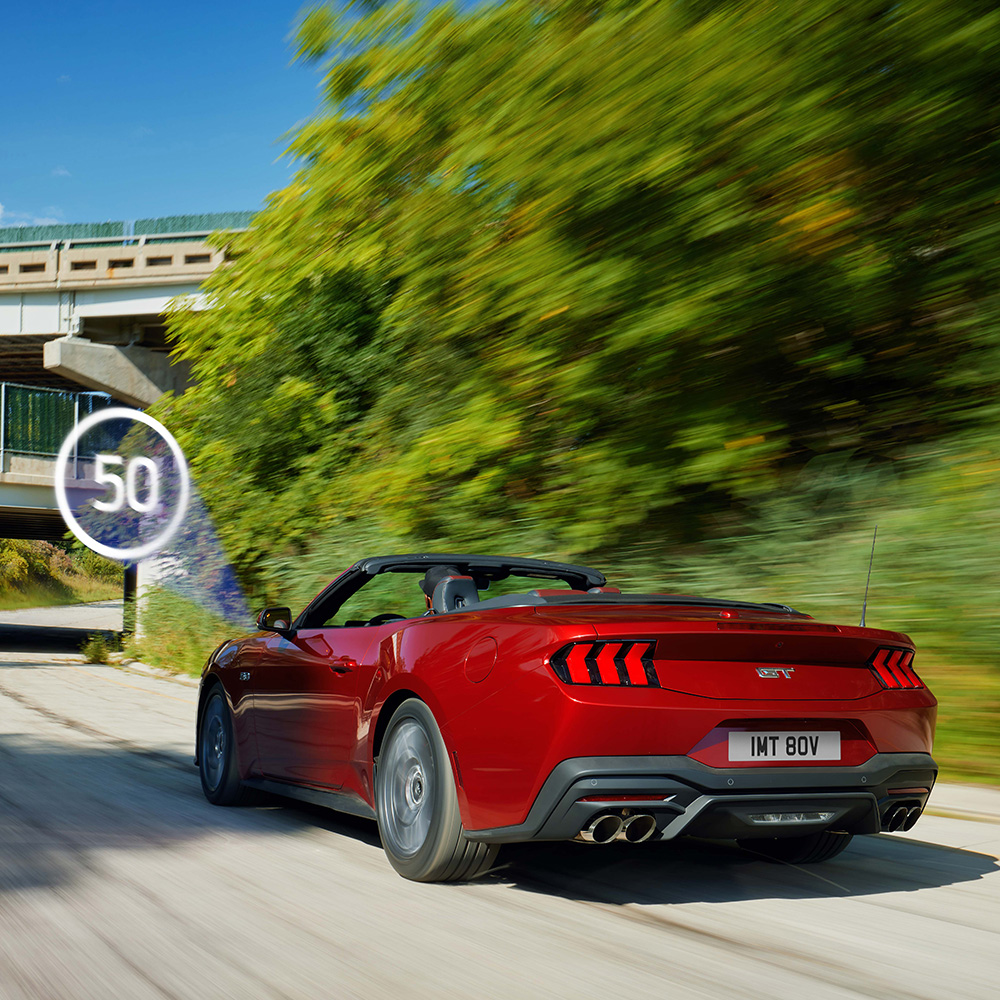 Ford Mustang rossa mentre passa accanto a un cartello stradale