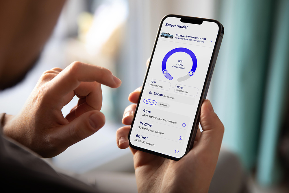 Una persona tiene in mano uno smartphone che mostra l'app Ford con l'interfaccia di avanzamento della ricarica EV.