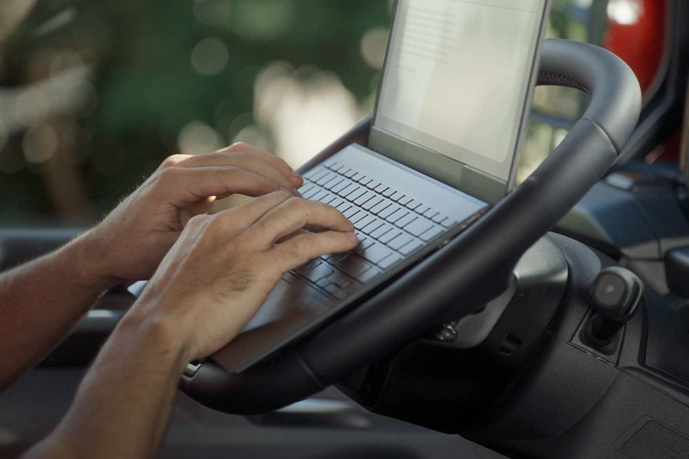 Le mani di una persona digitano su un computer portatile posizionato sul volante pieghevole del Ford Tourneo Custom.