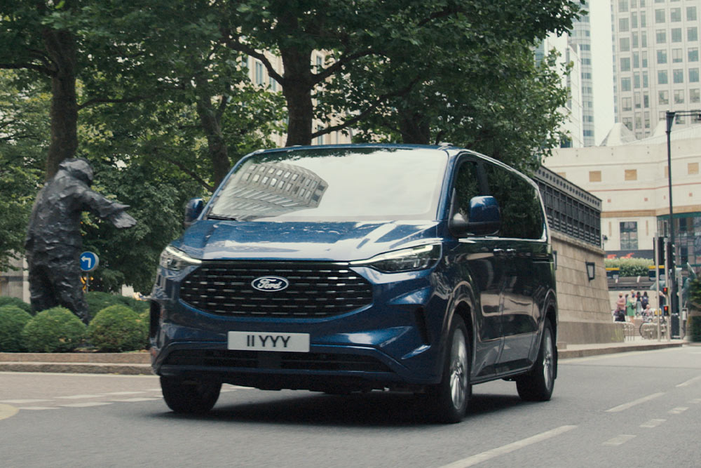 Un Ford Tourneo Custom blu percorre una strada cittadina.