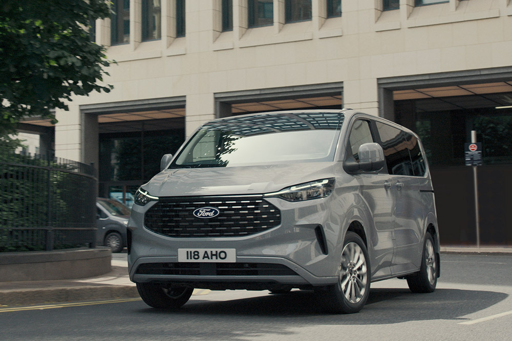 Un Ford Tourneo Custom argentato percorre una strada cittadina.