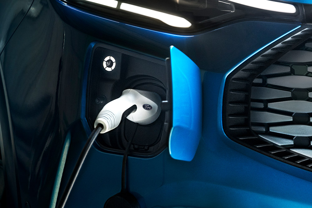 Primo piano della porta di ricarica di un Ford Tourneo Cutstom blu con il cavo di ricarica collegato.