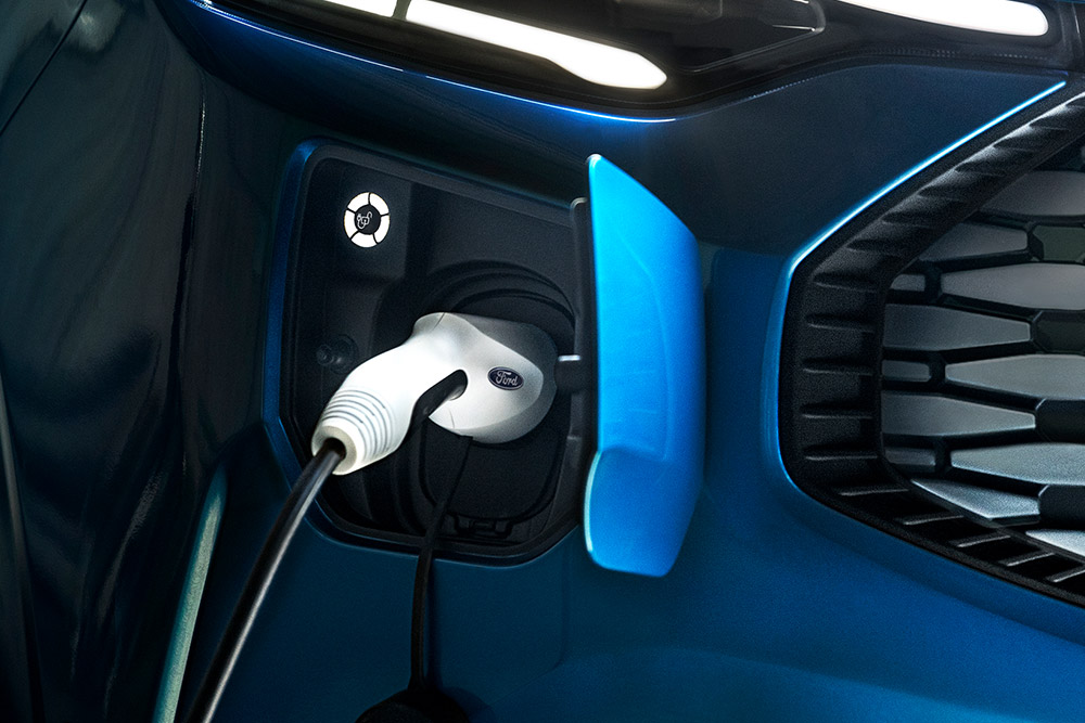 Primo piano di una porta di ricarica su un furgone Ford E-Transit blu con un cavo di ricarica collegato.