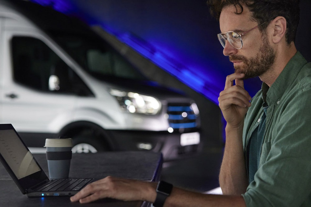 Un uomo che lavora con un PC portatile e un furgone Ford E-Transit sullo sfondo.