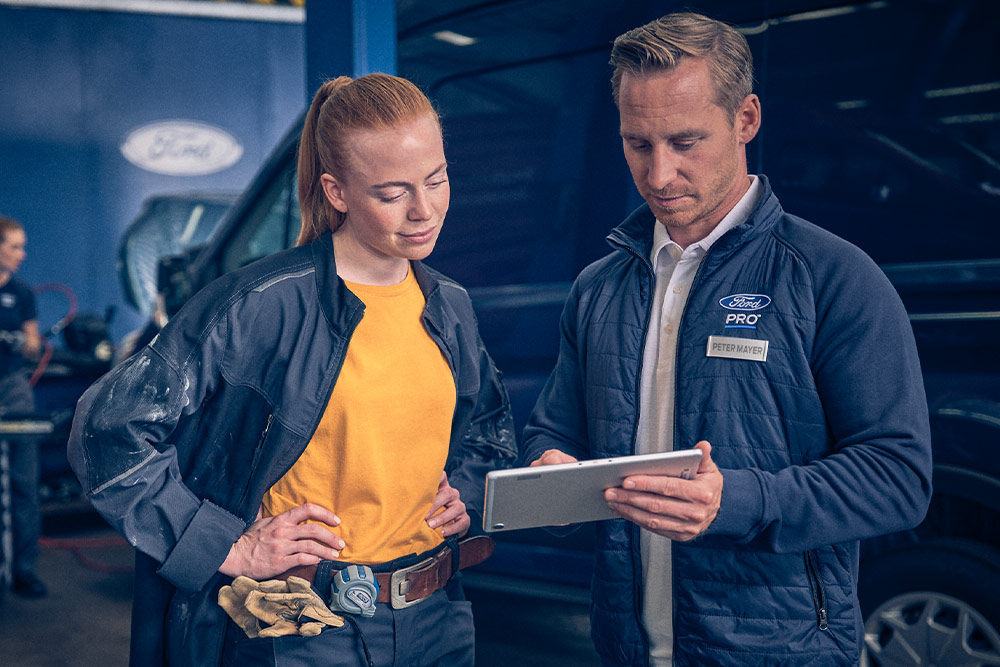 Due meccanici in un'officina che guardano un tablet di fronte a un furgone Ford E-Transit.