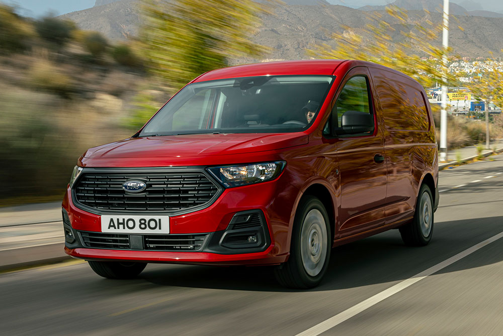 La griglia frontale e le luci automatiche di un Ford Transit Connect che percorre una strada.