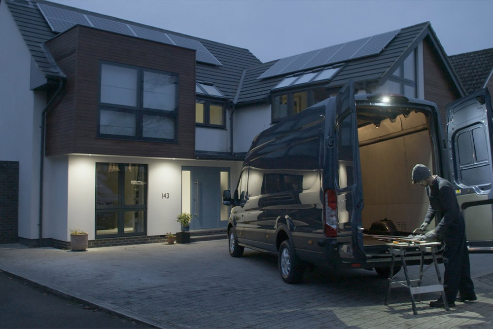 Un falegname lavora dietro a un furgone Ford Transit con le porte posteriori aperte di sera, illuminate dal faretto a LED.