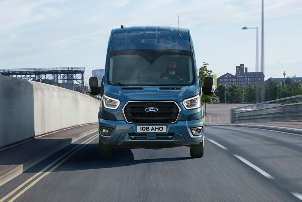 Vista frontale di un furgone Ford Transit versione blu che percorre una strada.
