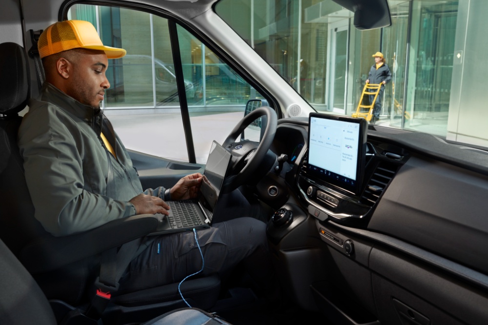 Un uomo seduto al posto di guida di un furgone Ford Transit, con un computer portatile.