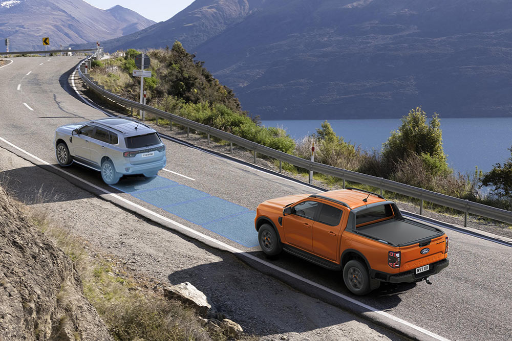Un Ford Ranger arancione utilizza il sistema di assistenza alla guida avanzato lungo una strada costiera. 