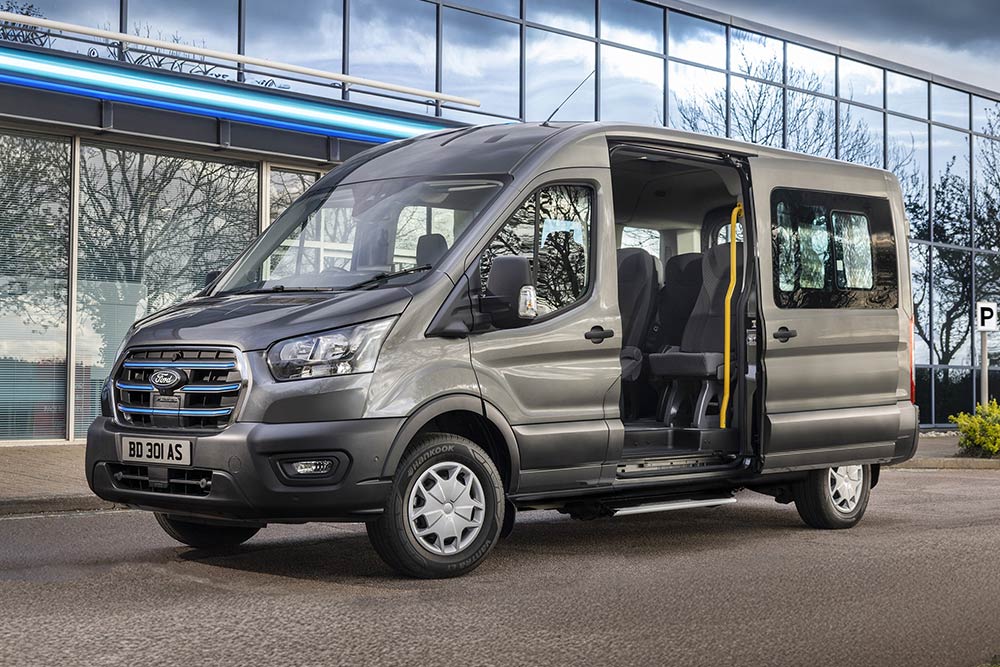 Vista laterale di un Ford Pro Transit grigio con le porte aperte, parcheggiato di fronte a un edificio moderno.