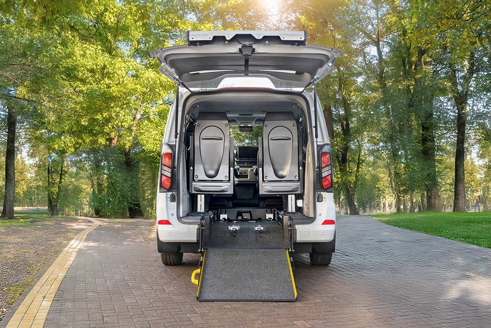 Vista posteriore di un Ford Transit Custom bianco con portellone aperto e rampa per sedia a rotelle dispiegata.