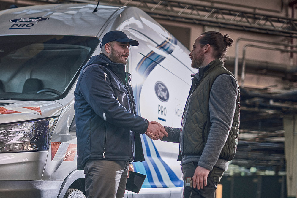 Un tecnico Ford Pro parla con un cliente, un furgone Ford Pro Mobile Service è visibile sullo sfondo.